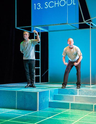 The school musical cast performs energetically on stage, showcasing colorful costumes and expressive movements.