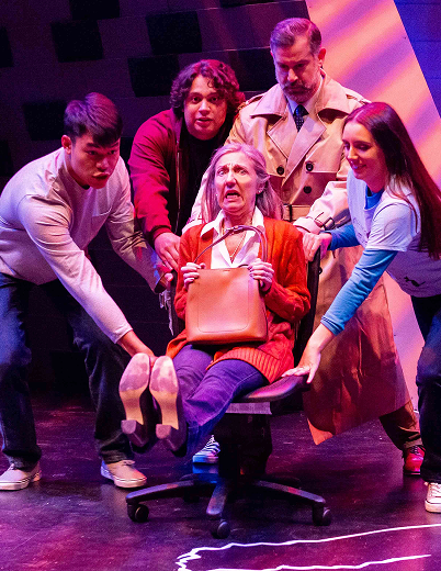 A group of people on stage, with a woman seated on a chair, engaged in a discussion or presentation.