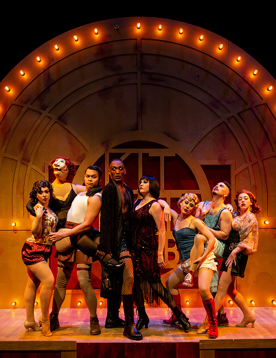 A group of women in colorful costumes poses together on stage, showcasing their outfits and smiles.