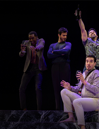 A group of men standing on stage, engaged in a discussion, with a spotlight illuminating them.