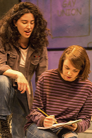 Two women sit on a bench, sharing a book and engaged in conversation, surrounded by a park setting.