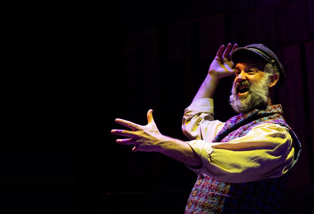 A man wearing a vest and hat holds a microphone, preparing to speak or perform