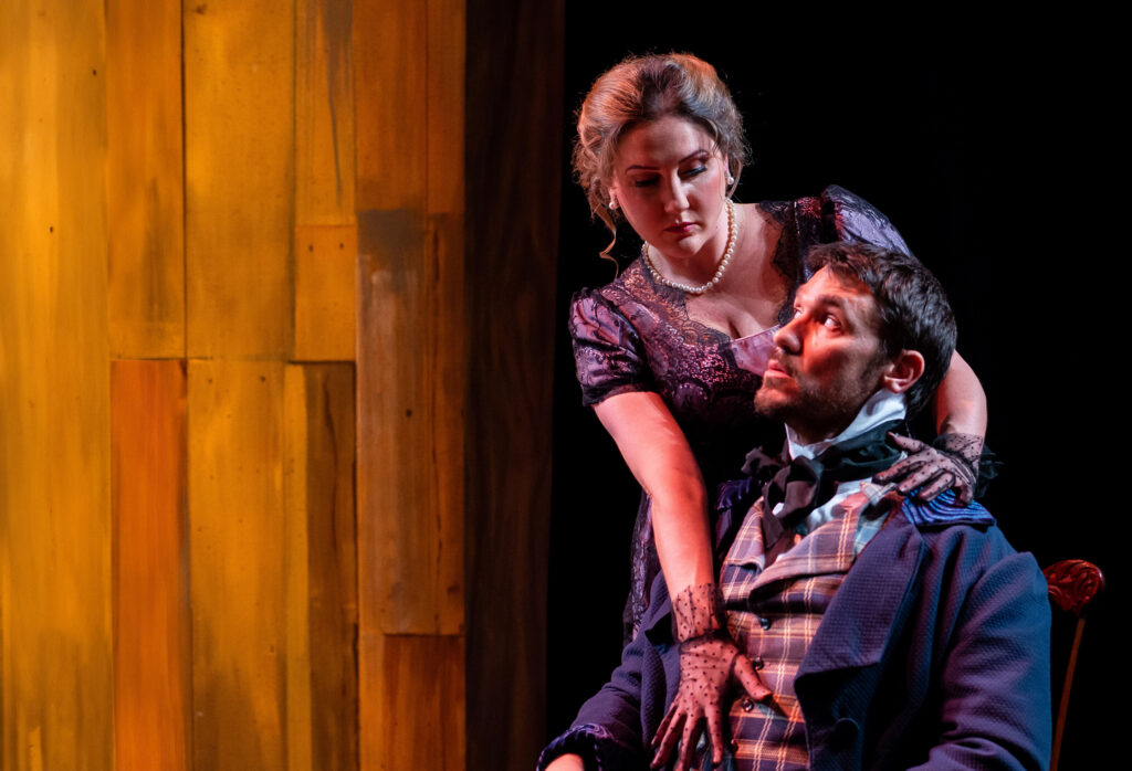 A man and woman in elaborate costumes perform on stage, showcasing their theatrical expressions and dramatic poses.