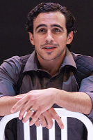 A man sits on a chair with his arms crossed, displaying a thoughtful expression.