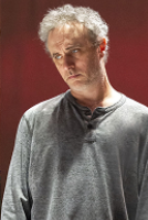 A man in a grey shirt stands beside a man in a black shirt, both facing the camera with neutral expressions.