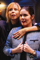 Two women embrace warmly in a theater, surrounded by dim lighting and empty seats.