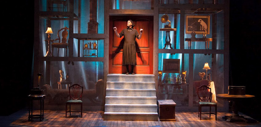 A woman stands confidently on stage, with an open door behind her, suggesting a moment of opportunity or transition.
