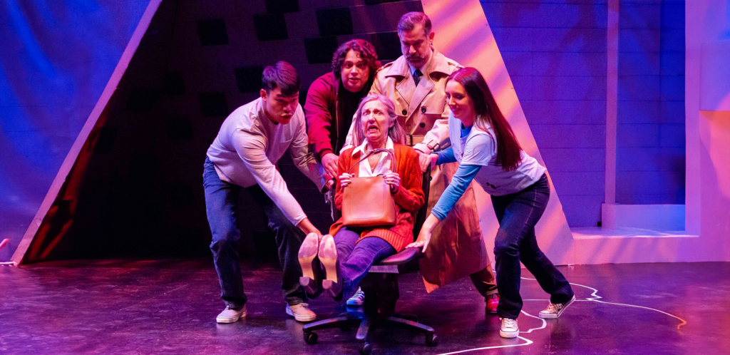 A group of people on stage, with a woman seated on a chair, engaged in a discussion or presentation.
