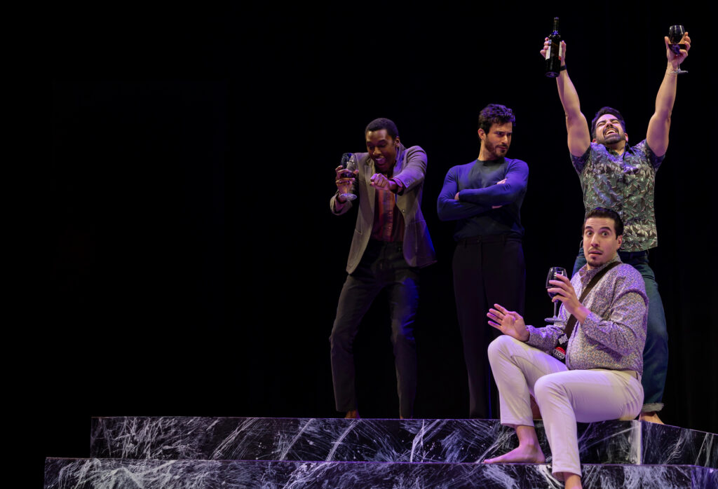 A group of men standing on stage, engaged in a discussion, with a spotlight illuminating them.